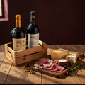 Gourmet wine and charcuterie pairing featuring red and white wines in a wooden crate, served with artisanal cheese, salami, and walnuts on a rustic table.
