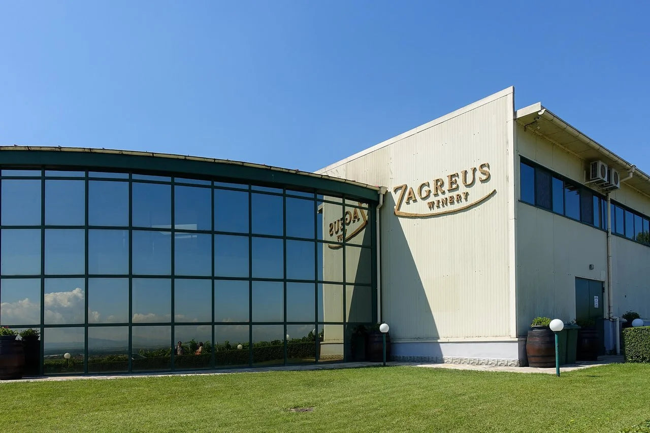 Modern architecture of Zagreus Winery featuring a large glass facade and branded signage under a clear blue sky.
